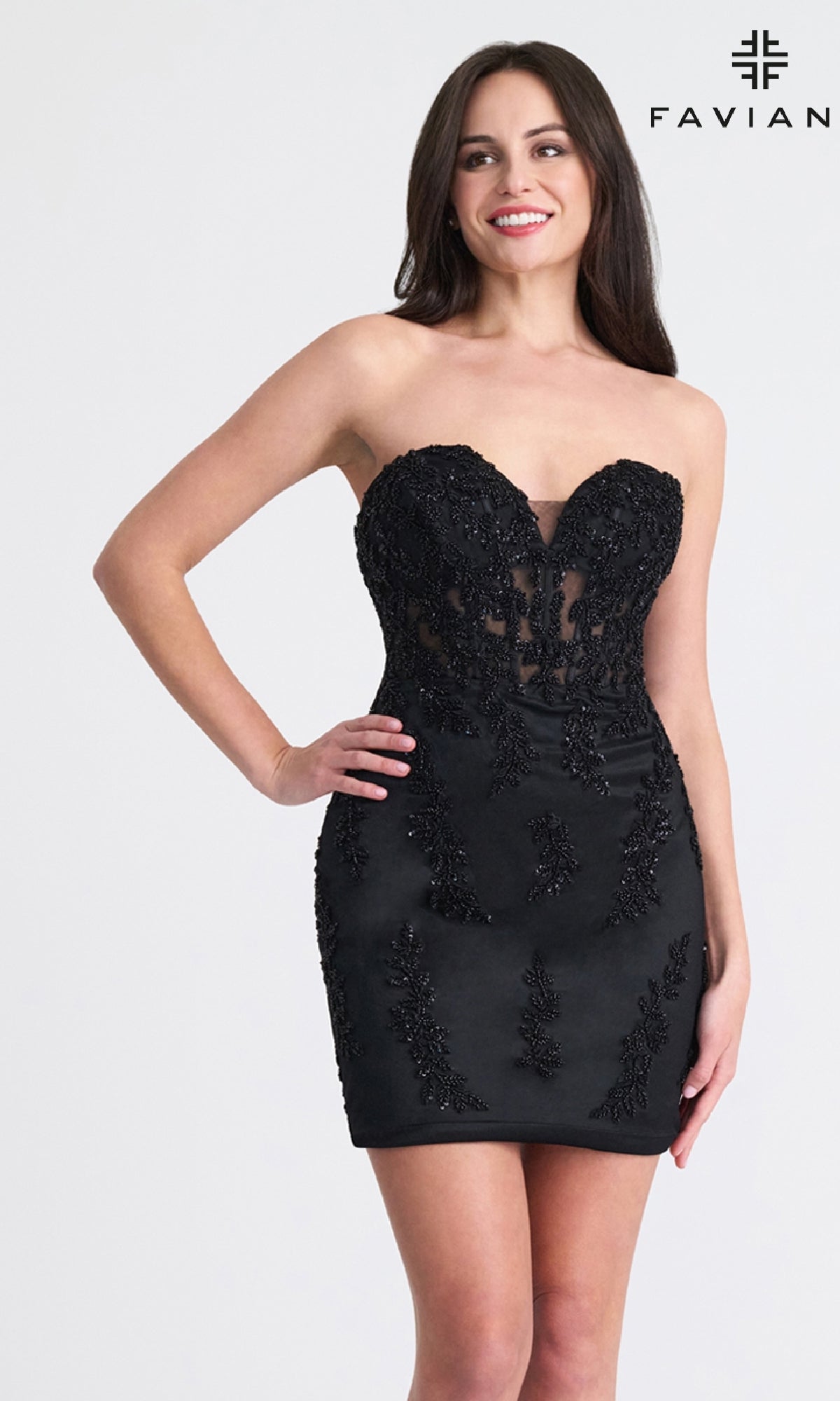 A woman wears the Strapless Short Corset Hoco Dress: Faviana 11317, featuring lace and bead embellishments, standing and smiling against a plain background with the Faviana logo in the top right corner.